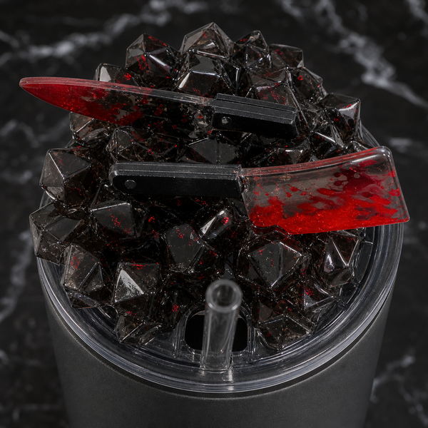 Close detail of smoky black resin ice tumbler lid with red-splattered miniature knife and cleaver charms