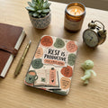 Journal, pen, candle, and alarm clock surround a planner declaring "Rest is Productive."