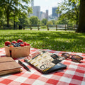 Picnic blanket with e-reader, journal, sunglasses, and berries with city skyline background.