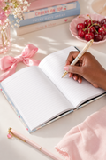 Hand holding a pen over an open notebook with cherry-themed decor