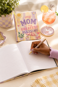 Person writing in personalized Mom keepsake journal with decorative card nearby