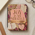 Journal with "JOY IS MY STRATEGY" and decorative crown, gems, and pearls.
